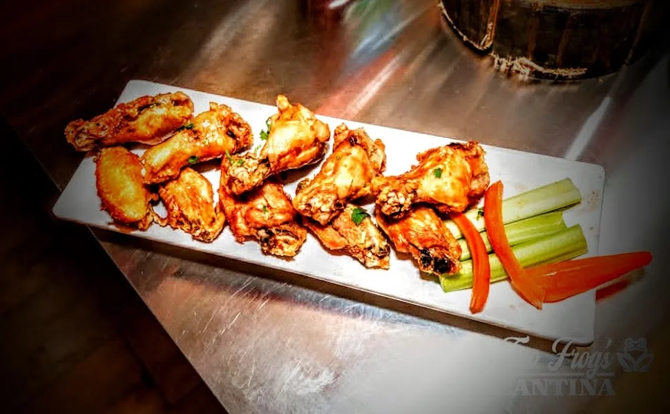 A rectangular plate holding a variety of chicken wings, accompanied by celery sticks and carrot slices.