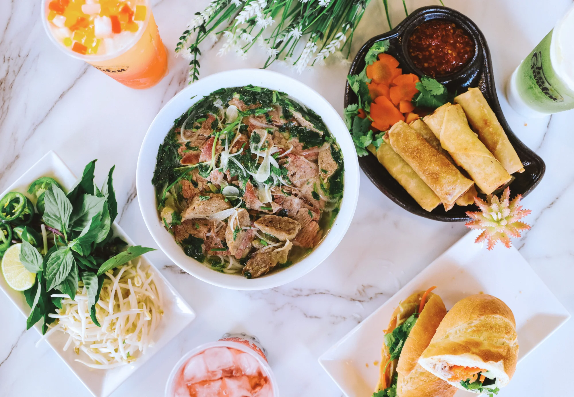Individual portions of eggrolls, banh mi, pho and drinks ready for catering.