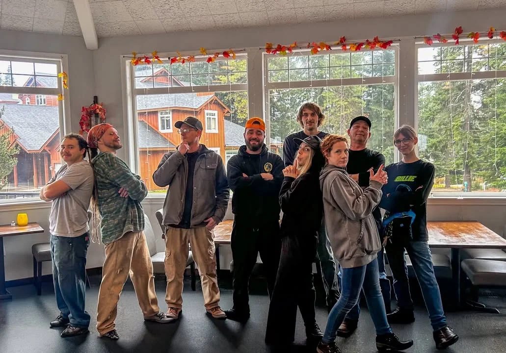 A group of individuals posing together with playful expressions in a cozy indoor setting with large windows.