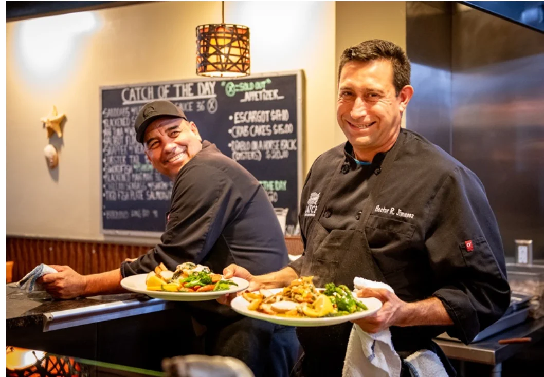 Chefs presenting seafood dishes in a cozy restaurant kitchen