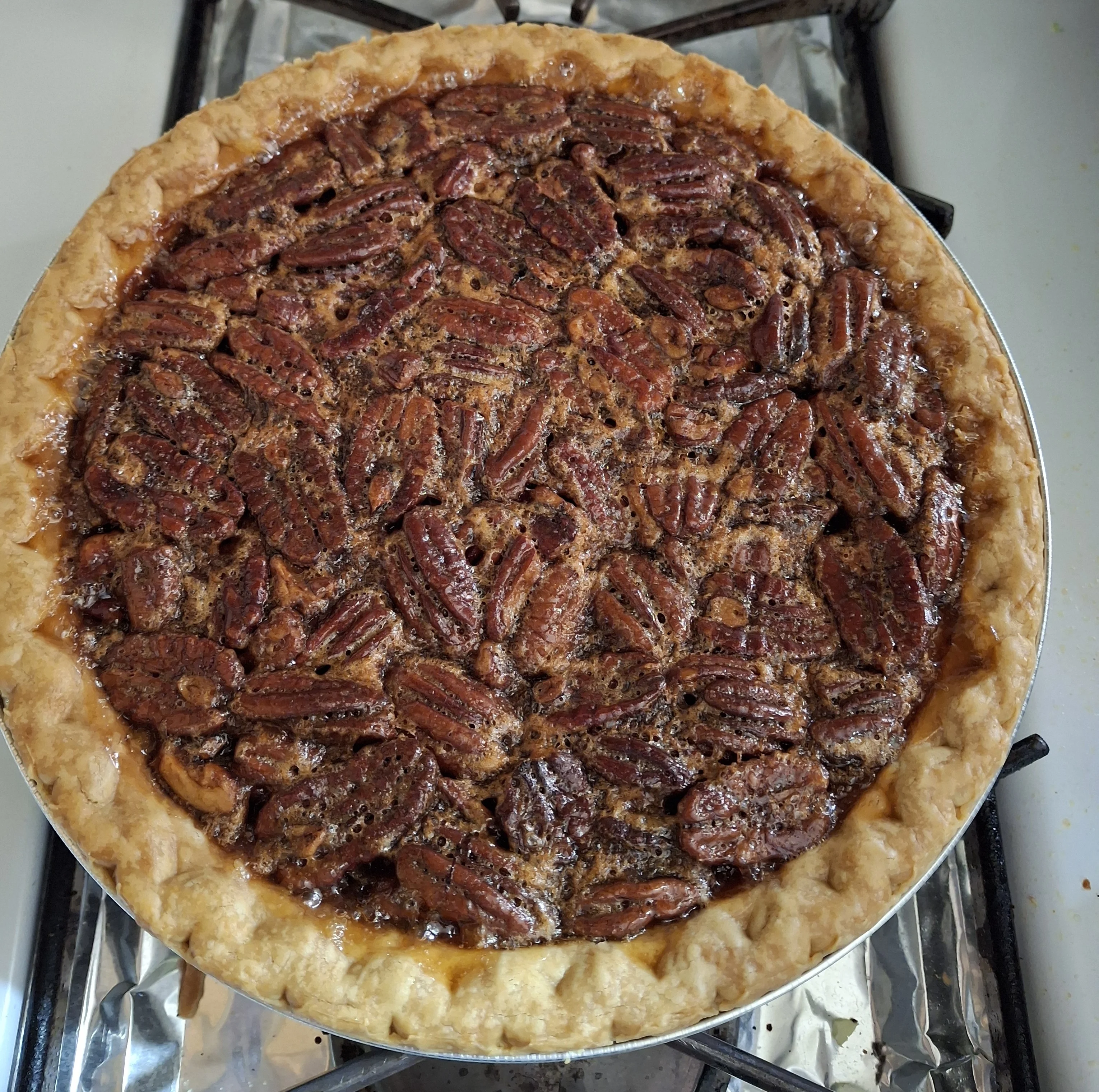 A pecan pie filled with whole pecans and a glossy syrup, inside a round pie dish.
