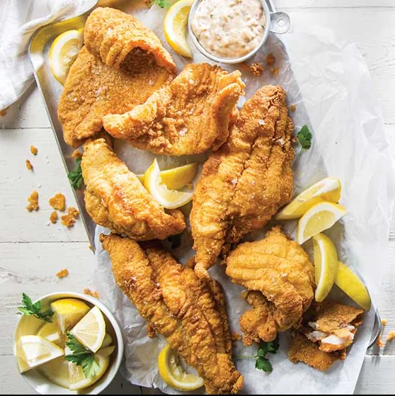 A platter of crispy fried fish fillets garnished with lemon wedges and a side of dipping sauce.