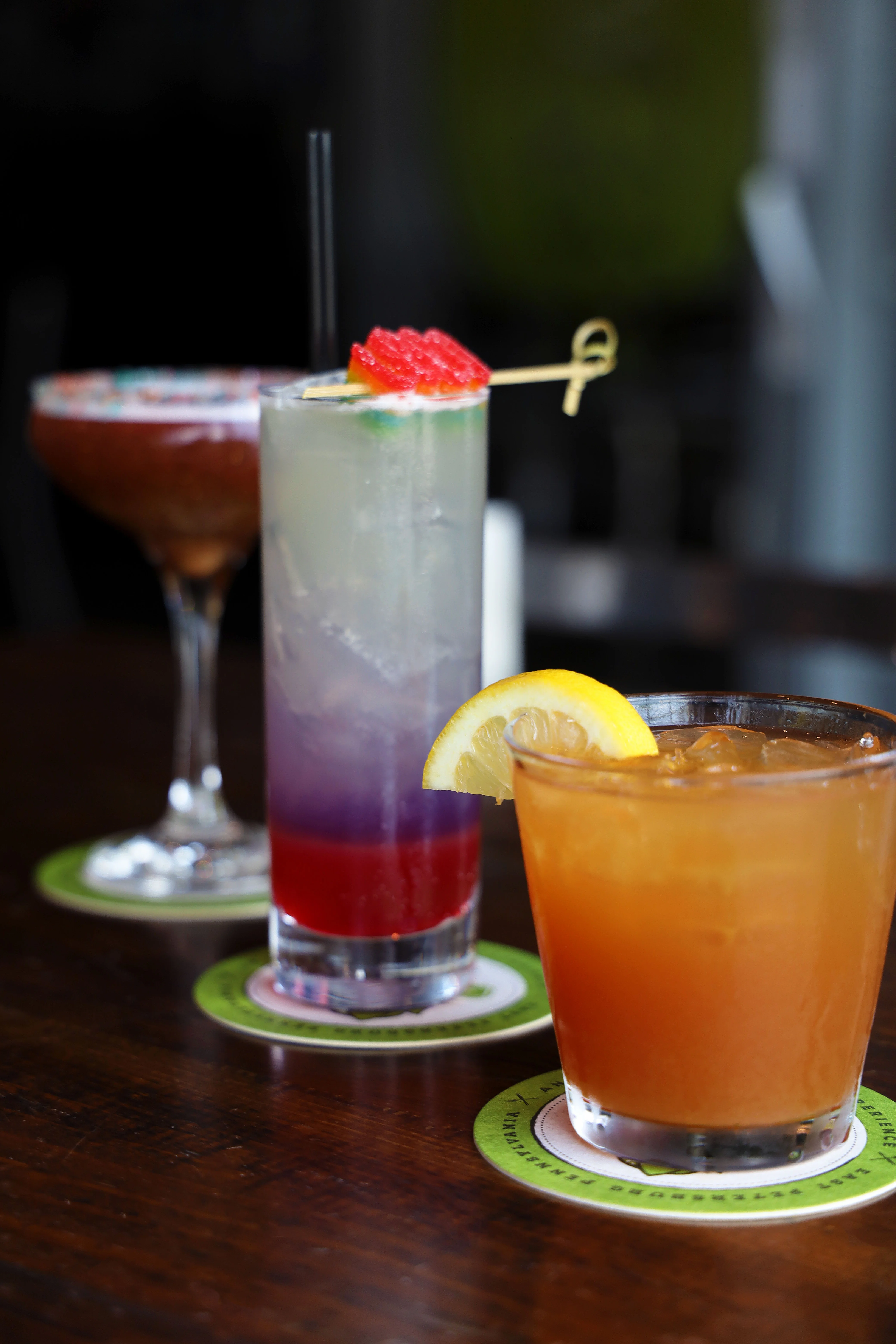 Three colorful cocktails on a table, showcasing vibrant garnishes.