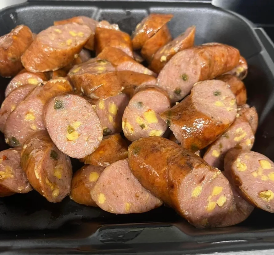A platter of sliced sausage pieces, showcasing a smoky roasted appearance with visible ingredients.