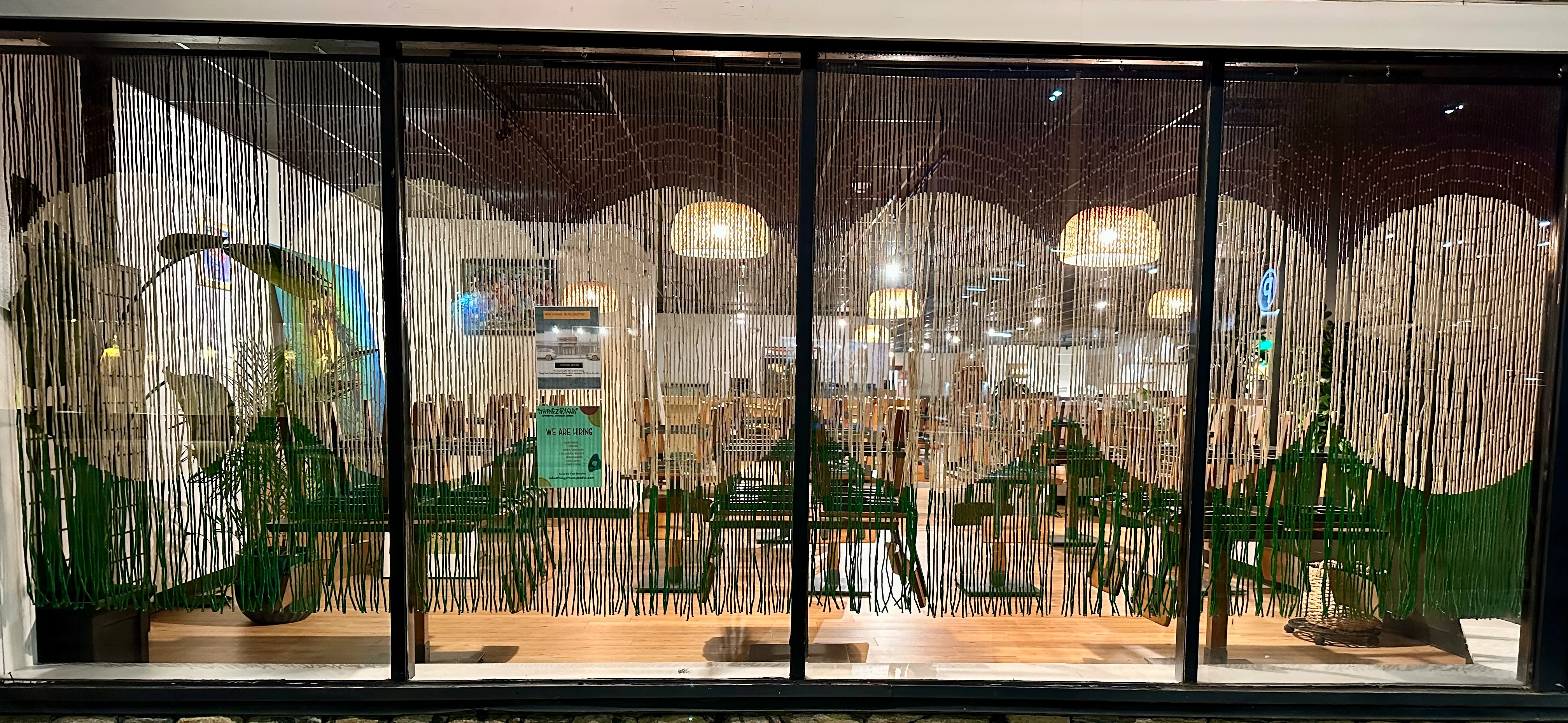 Restaurant window with decorative hanging strands and green accents.