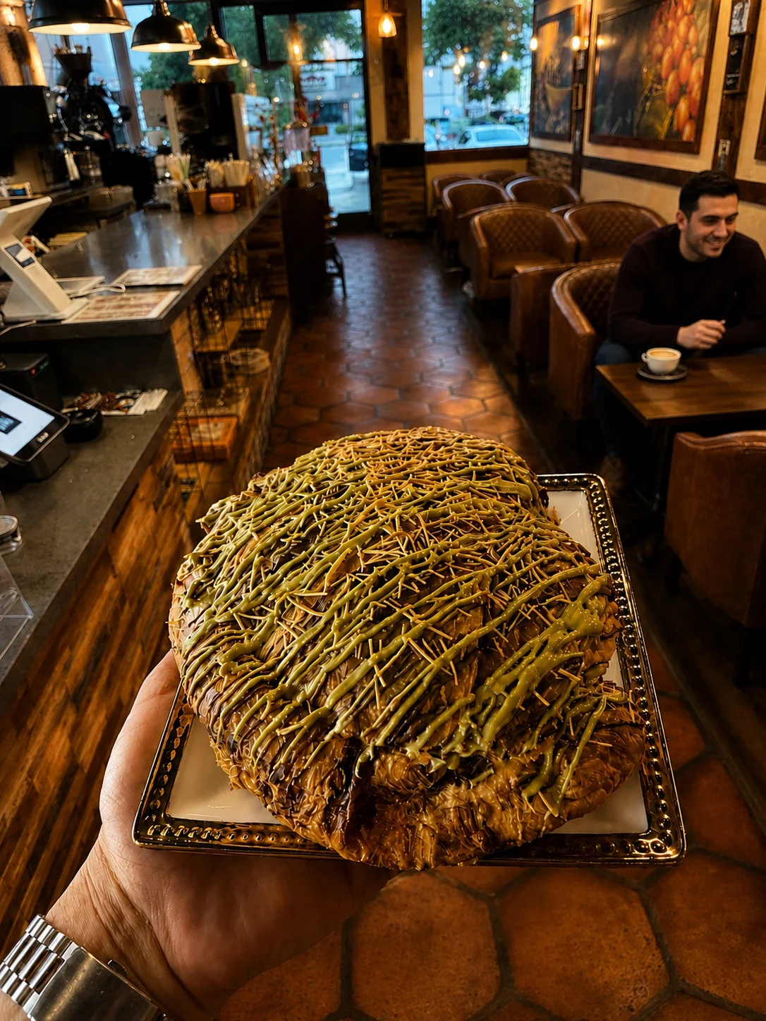 A large pastry with green drizzle, held in a cafe setting.