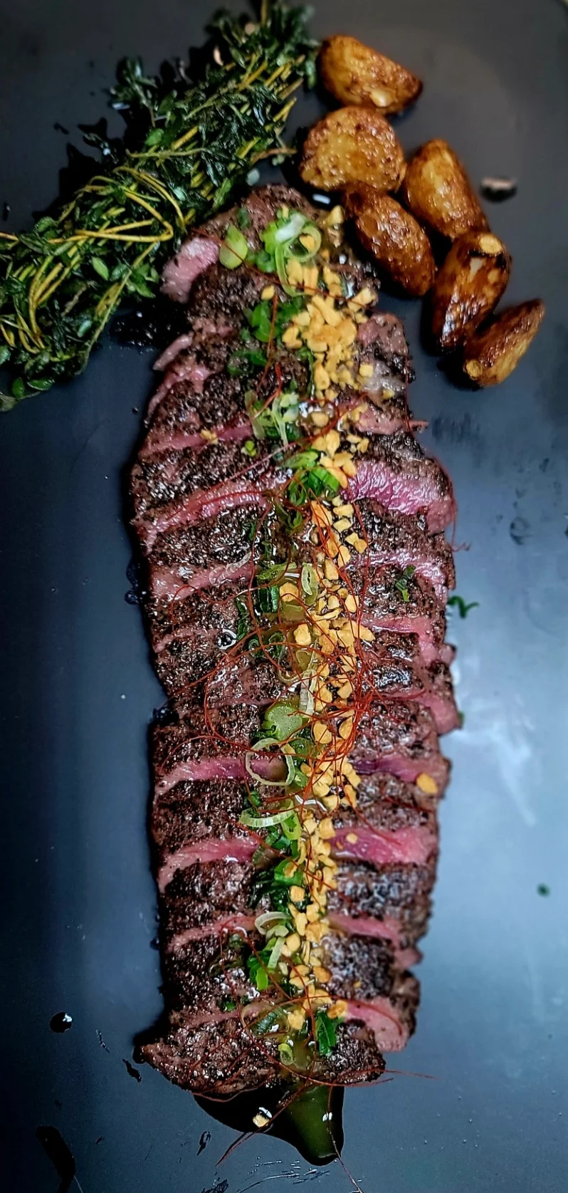 Grilled steak with herbs and garnishes on a black plate