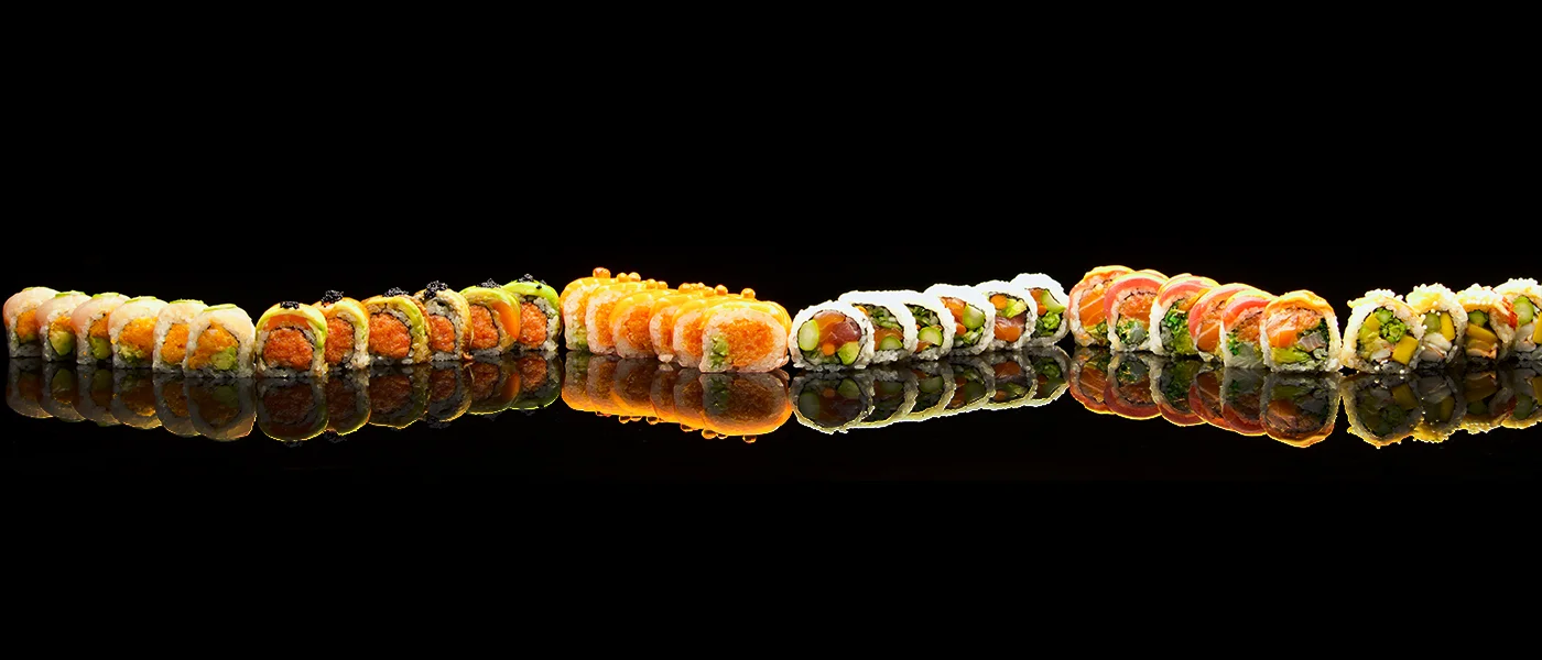 A variety of sushi rolls displayed on a reflective surface.