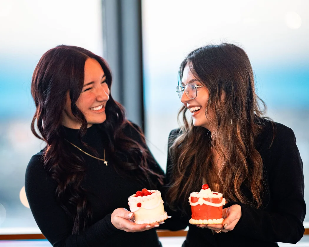 Two friends joyfully holding decorated cakes in a modern setting