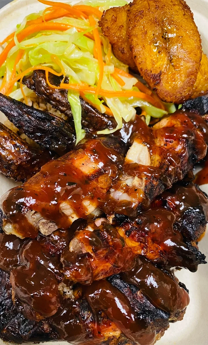 A plate of grilled chicken covered in barbecue sauce, accompanied by fried plantains and a fresh vegetable salad.