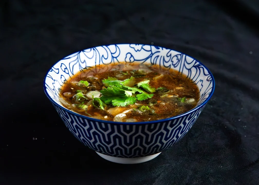 A bowl of soup garnished with fresh cilantro and herbs, resting on a dark surface.
