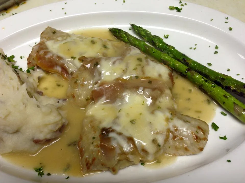 A plate featuring pork chops covered in a creamy sauce, paired with mashed potatoes and grilled asparagus on the side.