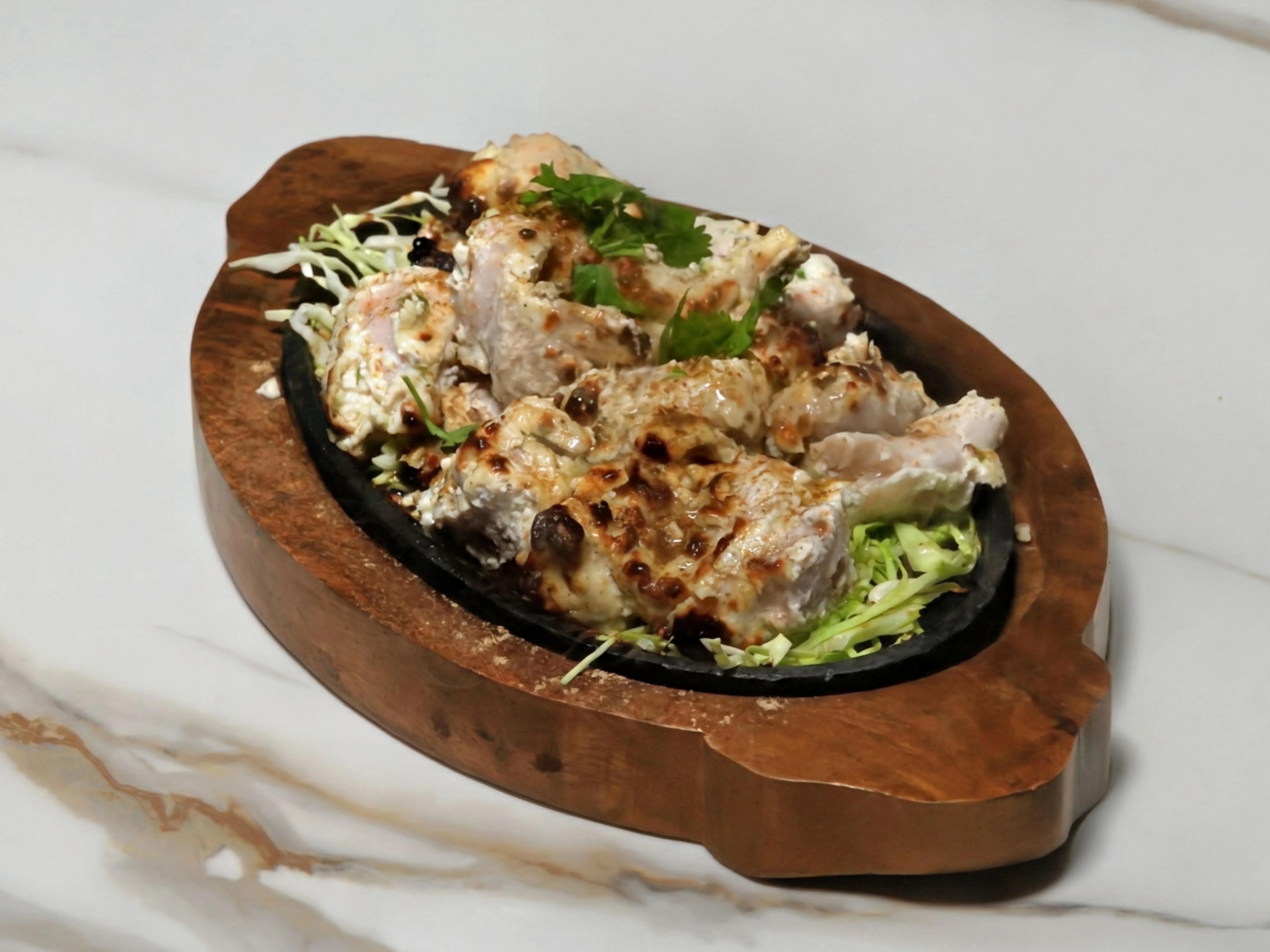 A serving of grilled chicken delicately placed on a bed of shredded cabbage, served on a wooden platter.
