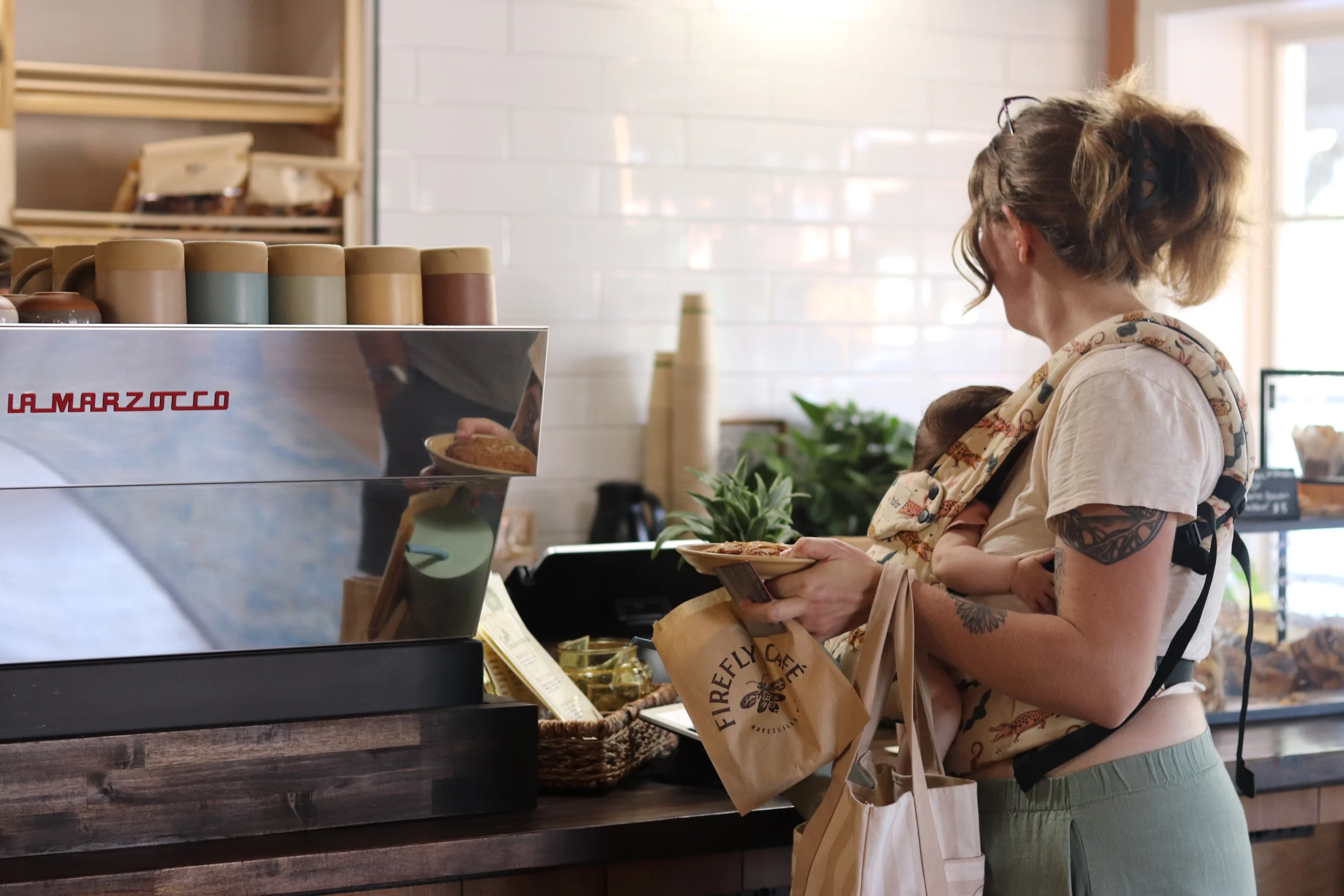 Two children are arranging letters on a sign board that reads 'THE FIREFLY CAFE COMING SOON.' The scene is set in a cozy space with wooden flooring.