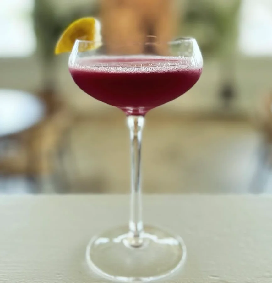 A vibrant cocktail in a coupe glass with a lemon garnish.