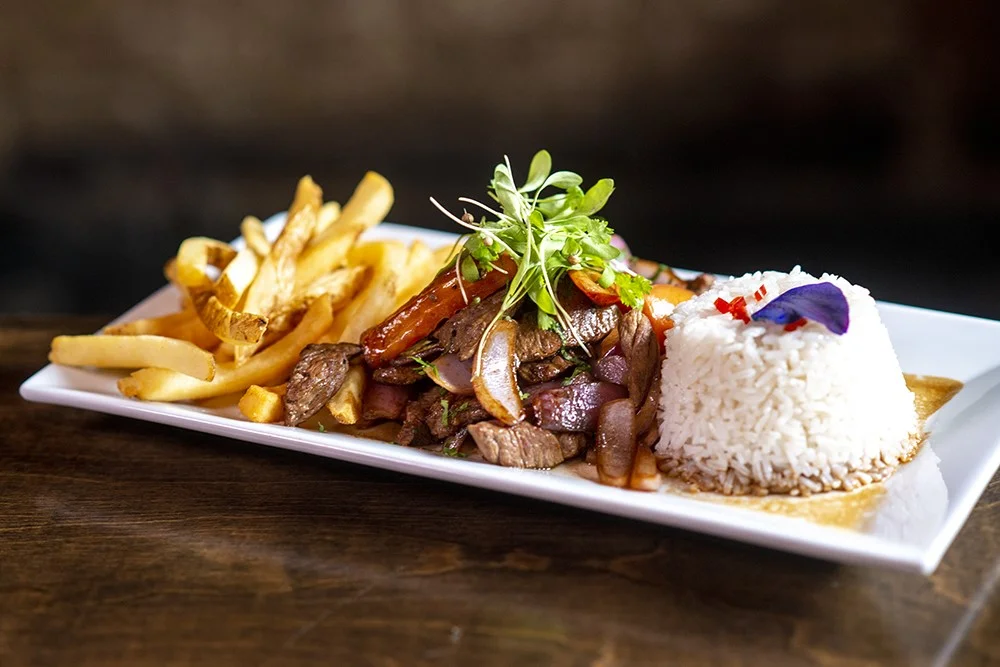 Peruvian lomo saltado with rice and fries on a white plate