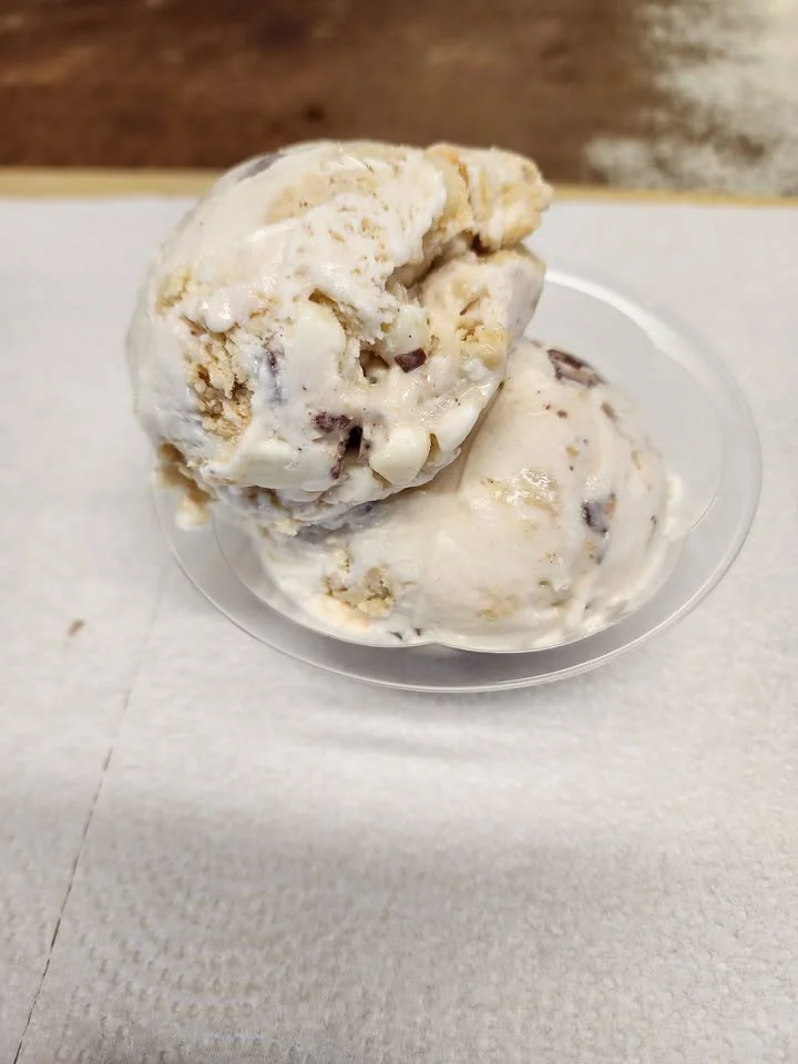 A dessert cup featuring two scoops of creamy ice cream, with cookies and chocolate chunks, served on a clear dish.