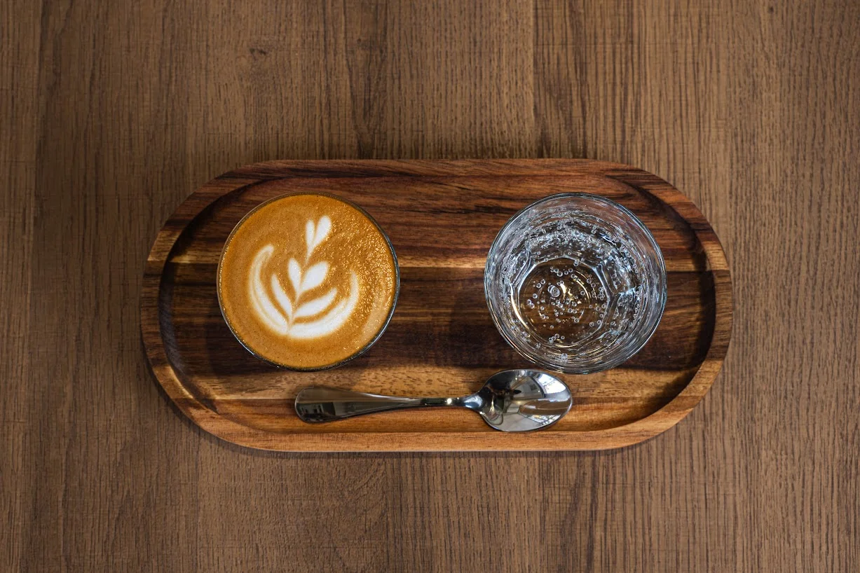Cappuccino with latte art, water, and spoon on a wooden serving tray