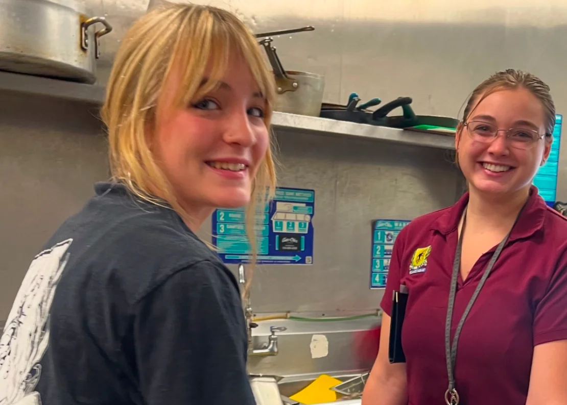 Two restaurant staff smiling in a busy kitchen