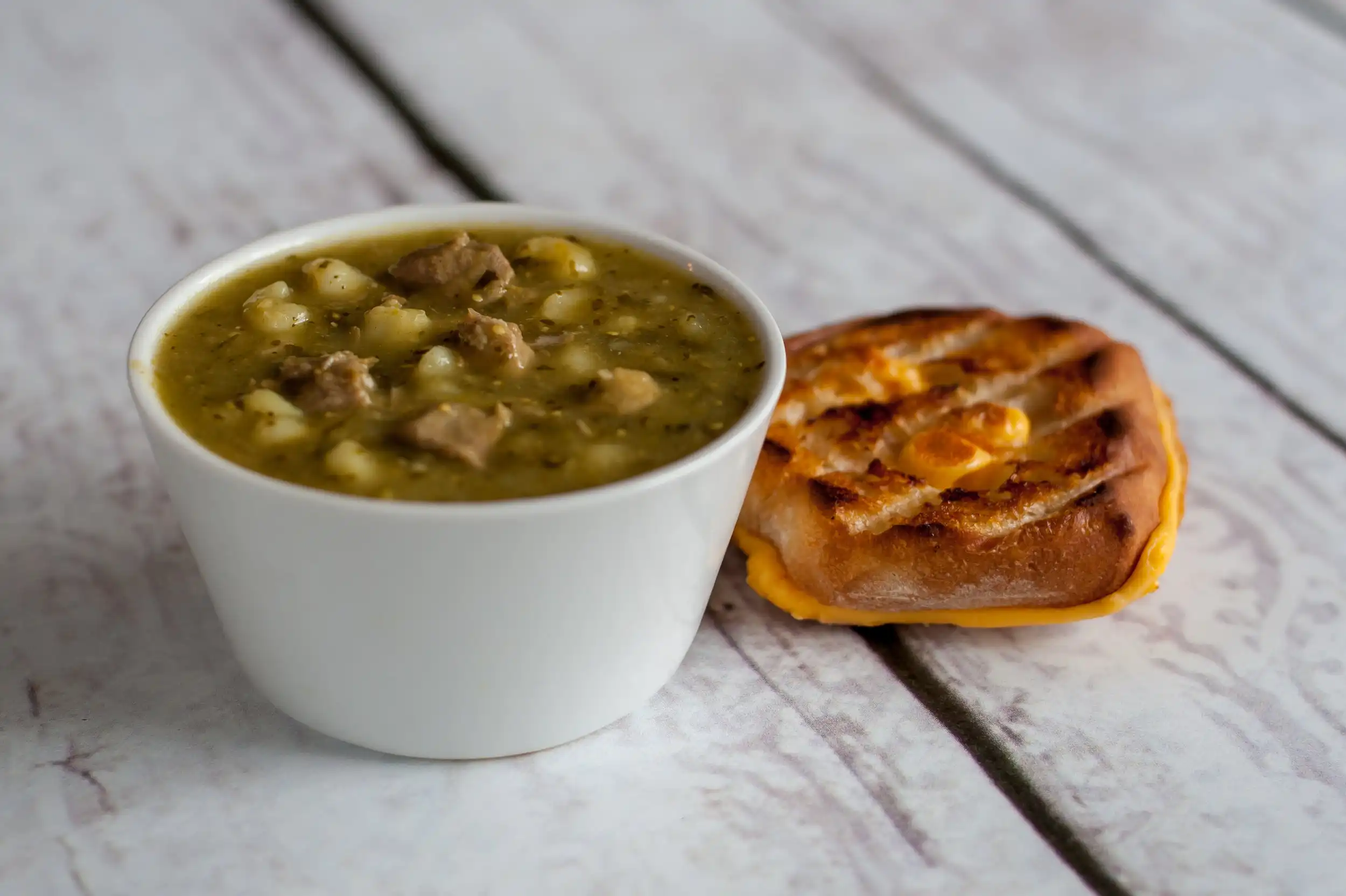 A bowl of warm Pork Chile Verde soup with a toasty grilled cheese sandwich.