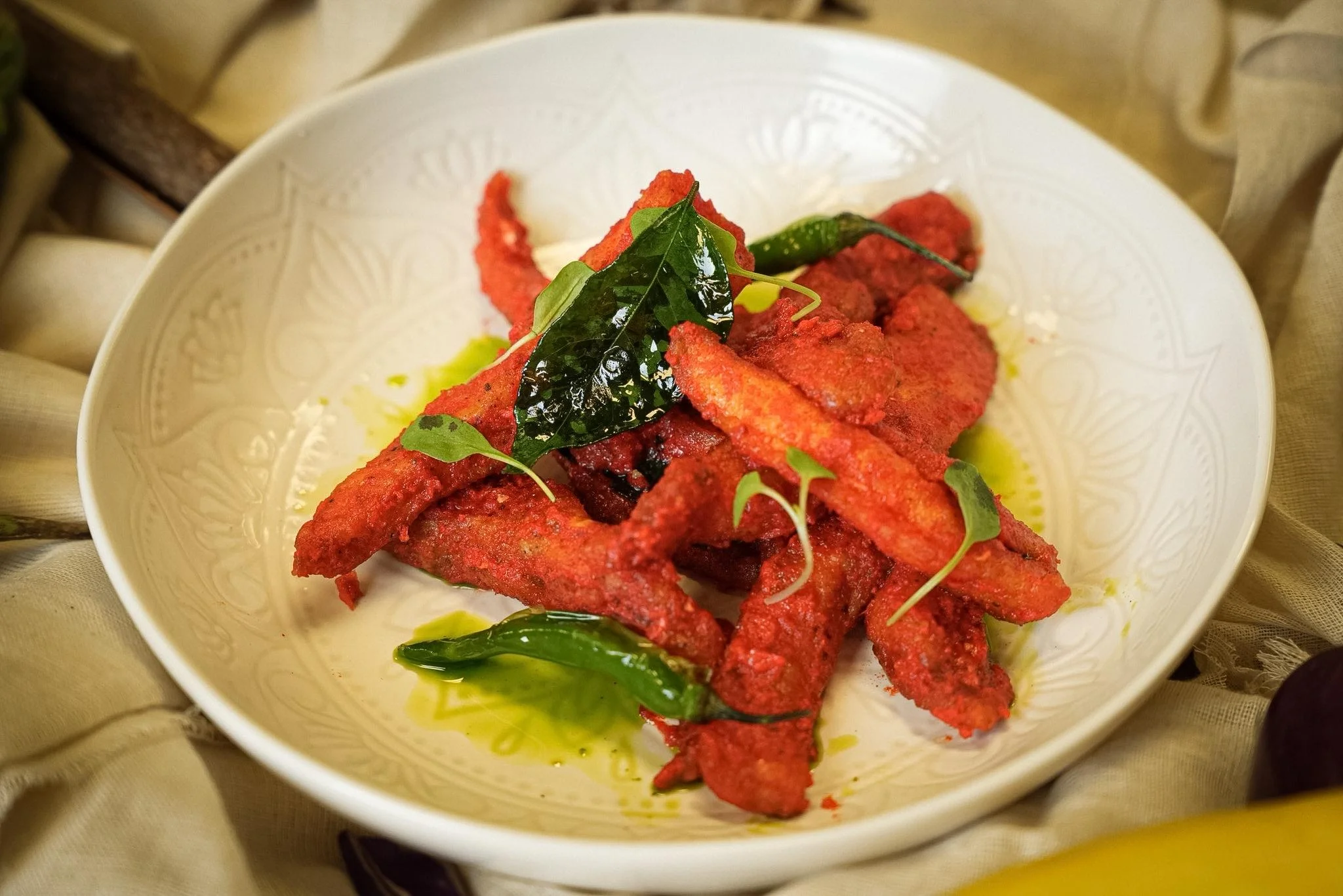 Crispy red fried vegetable strips garnished with fresh green leaves, presented in a decorative white bowl.