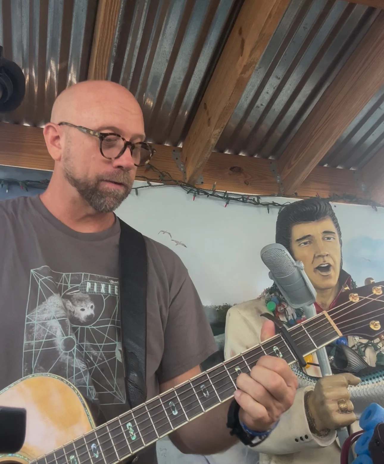 Musician playing guitar with Elvis statue in a lively setting