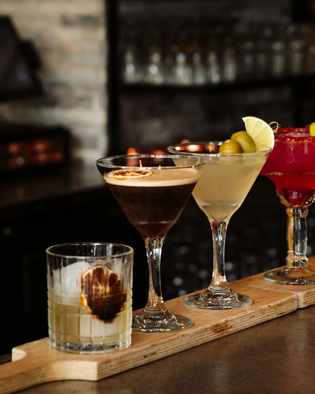 Assorted cocktails on a wooden flight at a stylish bar