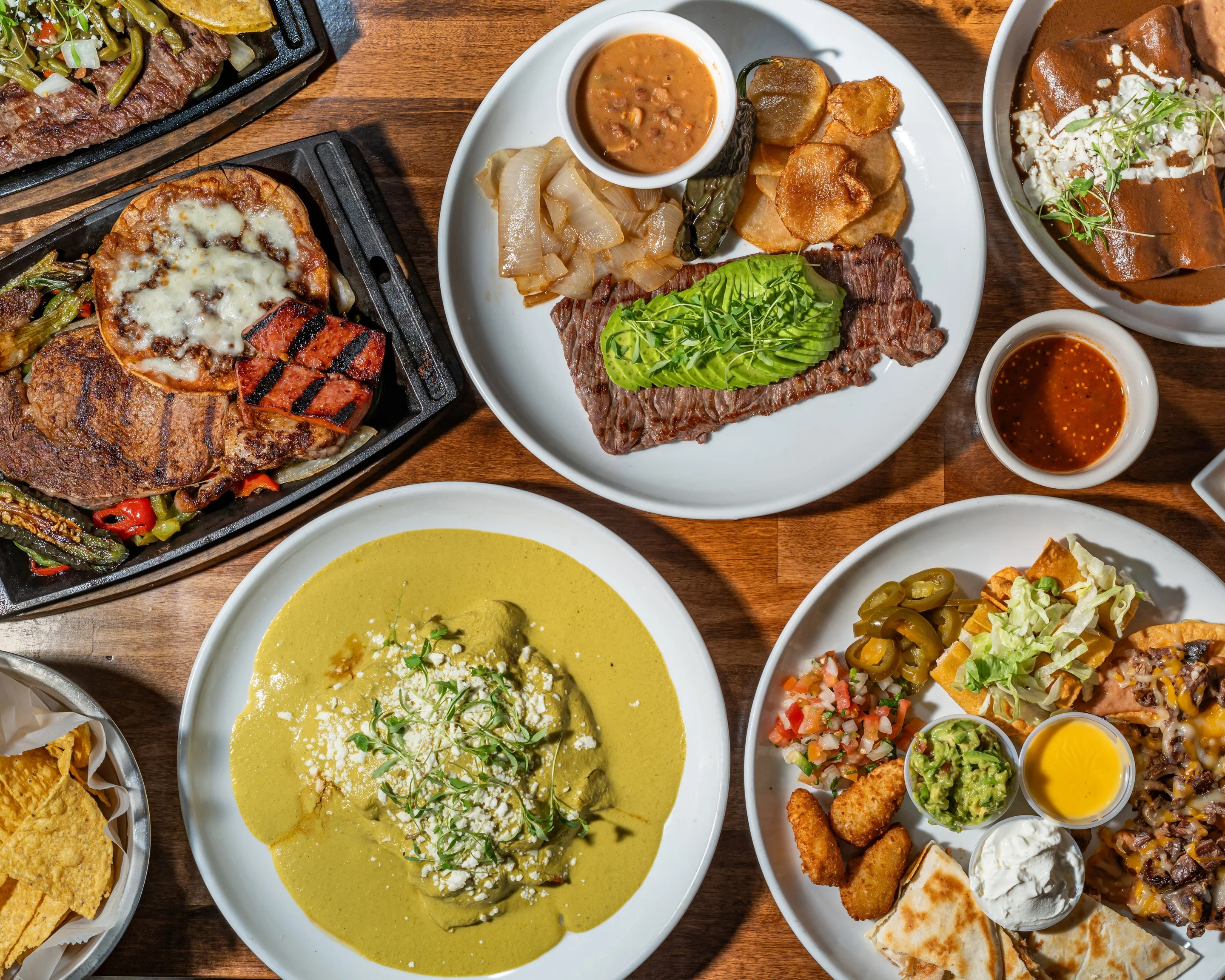 A colorful plate featuring a variety of Mexican dishes including nachos, taquitos, quesadillas, and sides of salsa and guacamole.