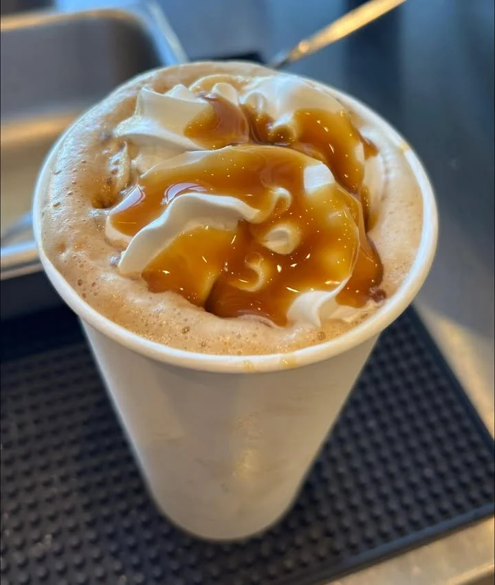 A cup of whipped cream topped with caramel sauce, sitting on a textured surface.