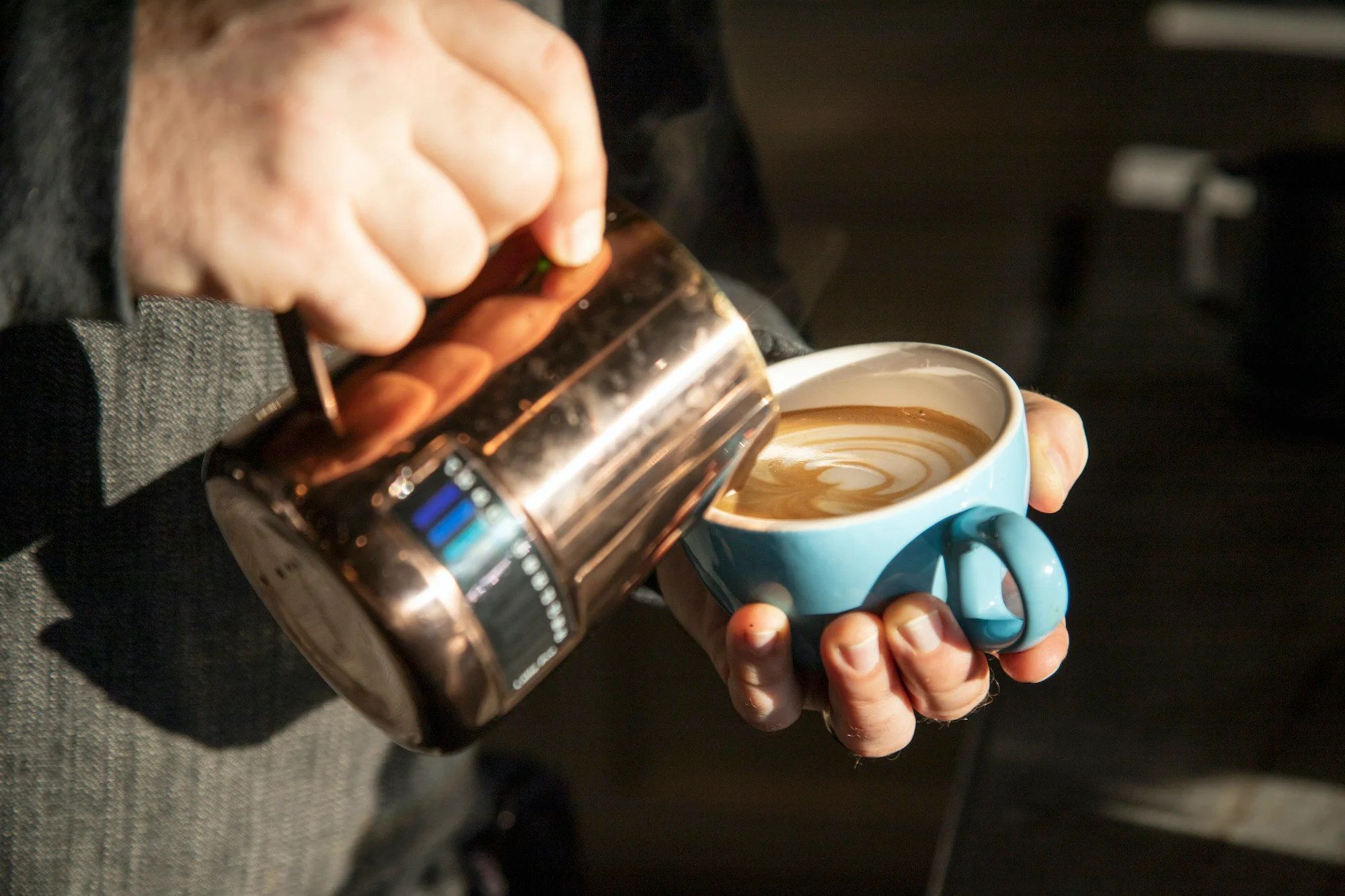 Barista pouring latte art into a blue coffee cup