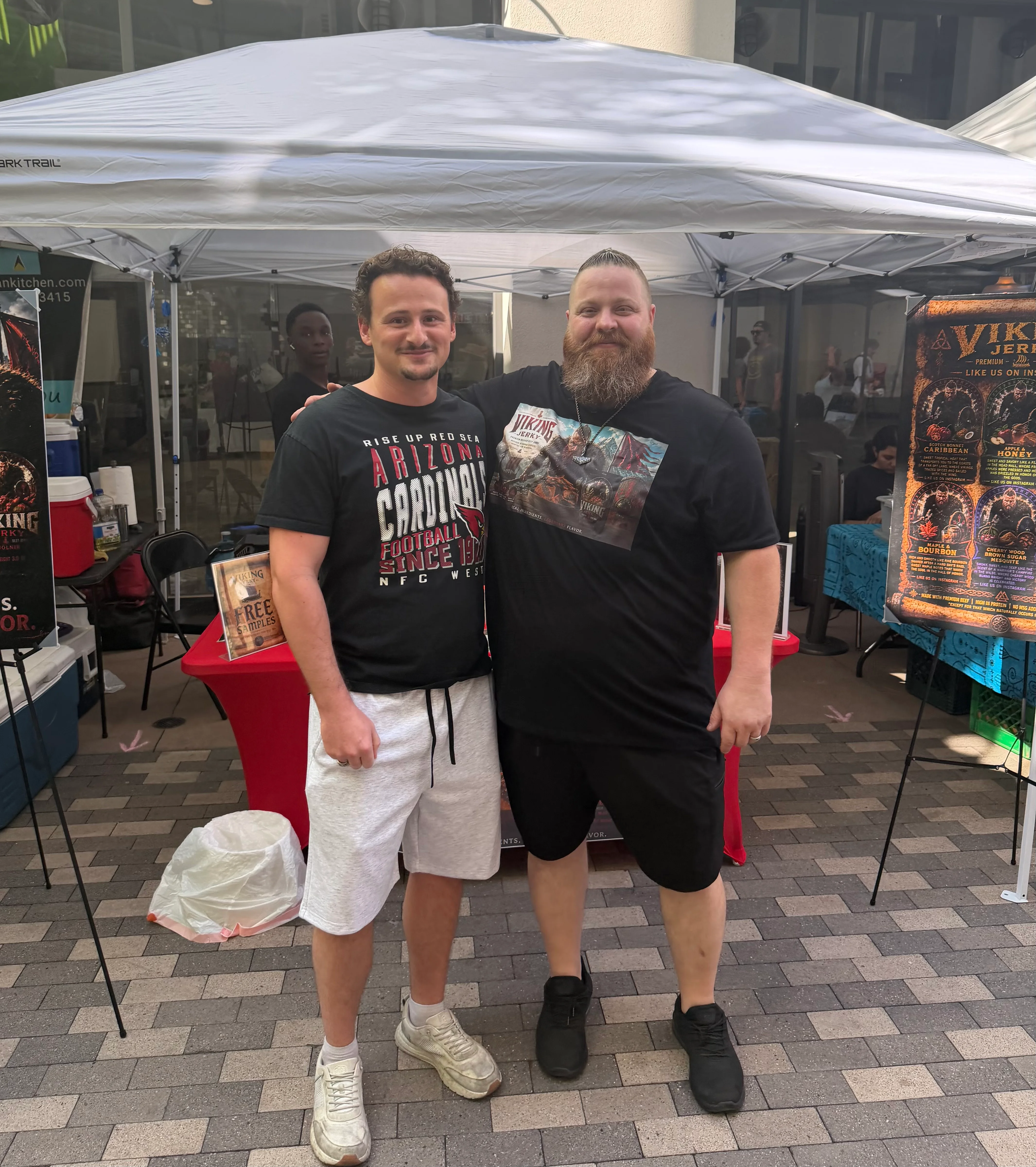 Two men posing at a food festival booth with promotional signage
