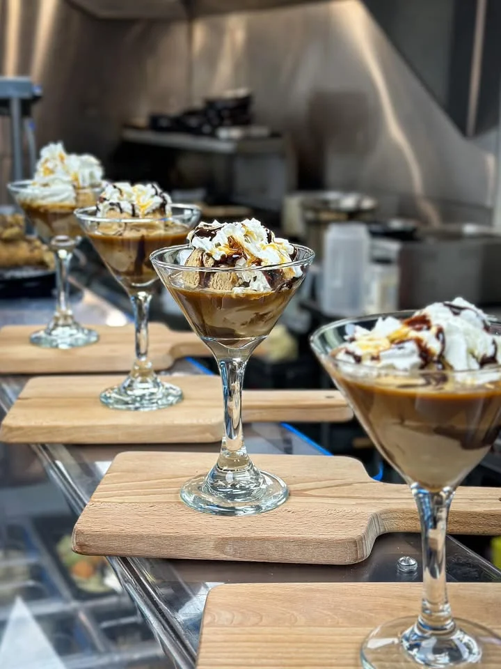 Elegant dessert presentation featuring mini desserts in martini glasses. Each glass is filled with chocolate ice cream, drizzled with caramel and topped with whipped cream.