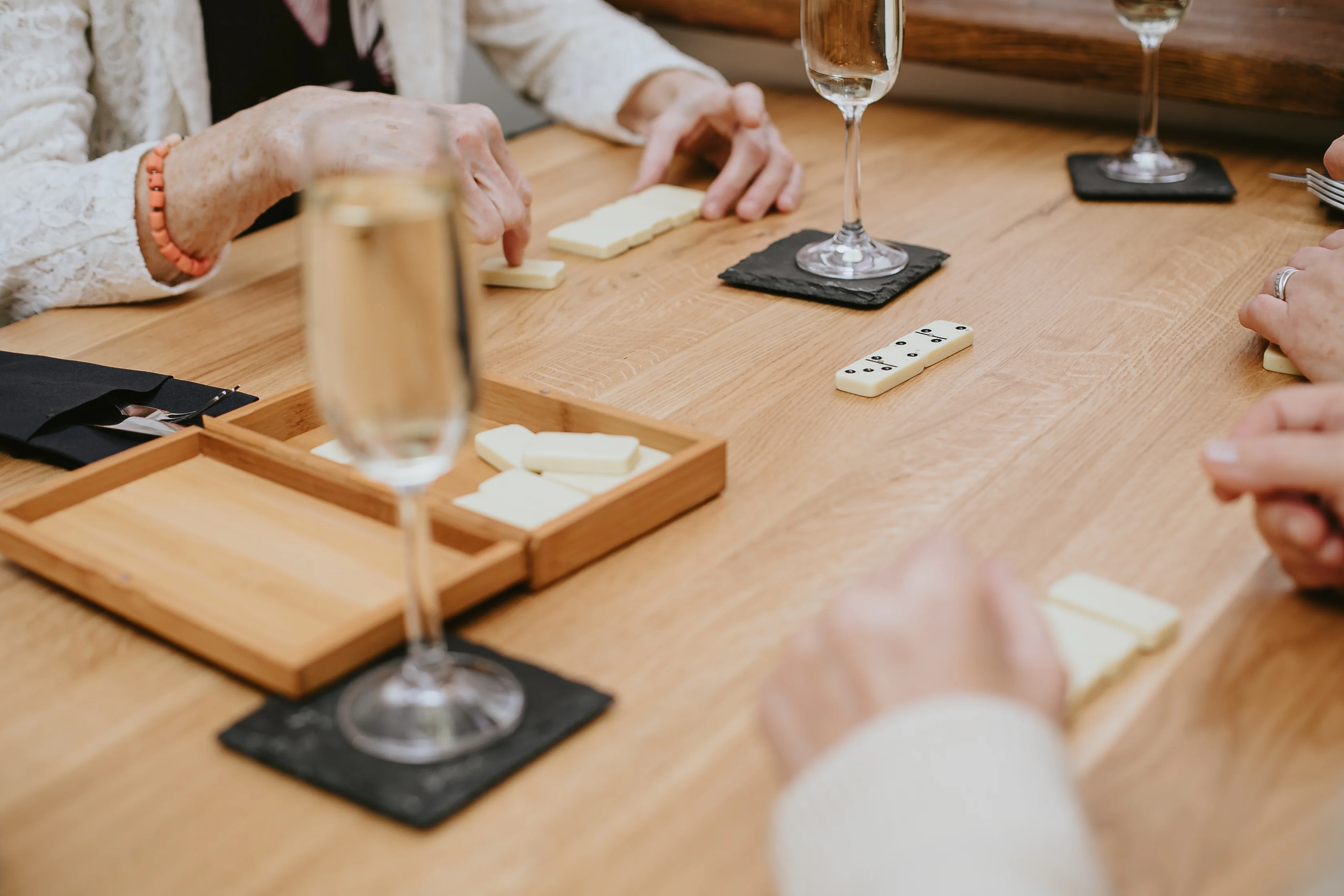 Group enjoying a game of dominoes with drinks on a wooden table