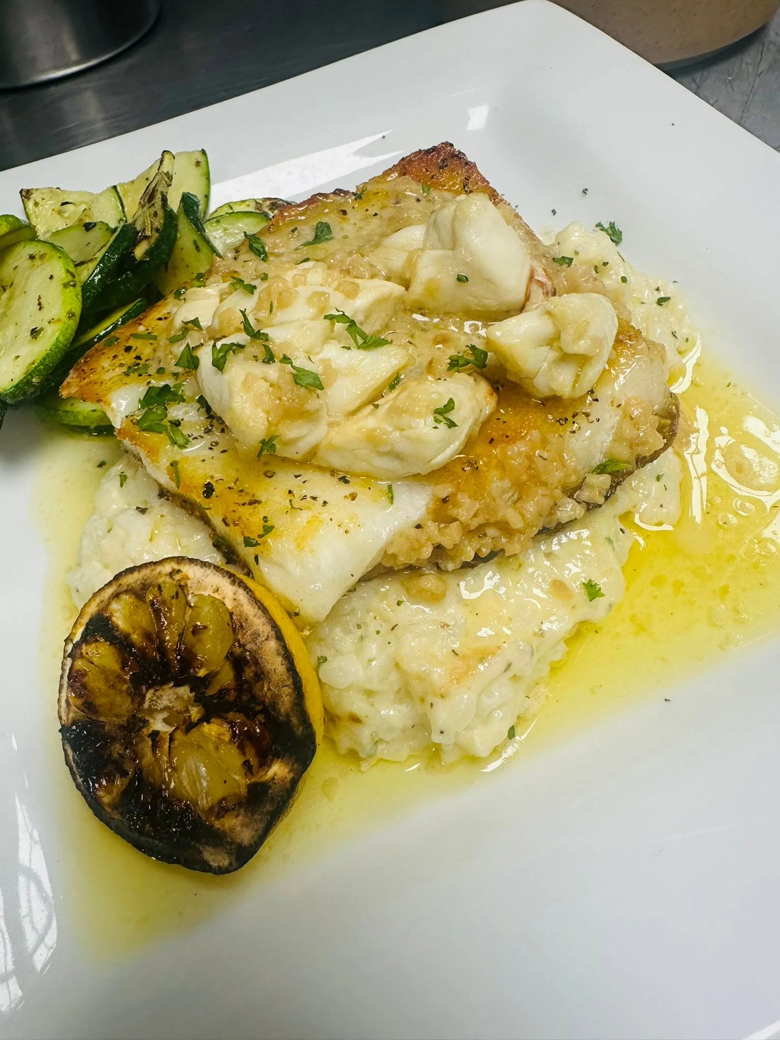 Pan-seared fish with crab on creamy risotto, garnished with grilled zucchini and lemon