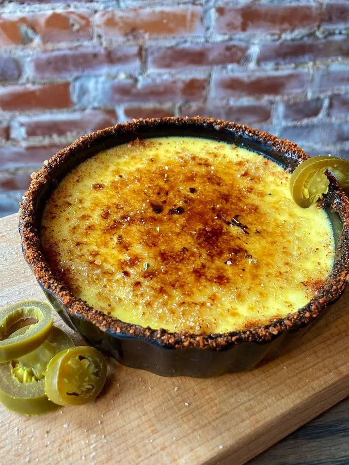 A creamy dessert topped with a caramelized layer and garnished with sliced pickled jalapeños.