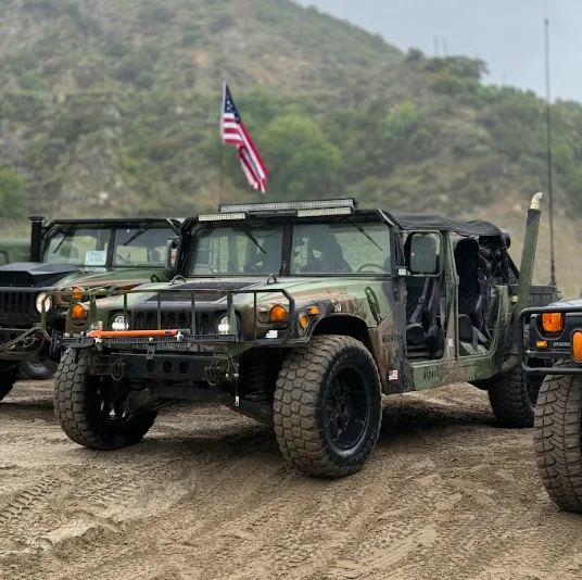 Military-style off-road vehicles with an American flag against a rugged hillside