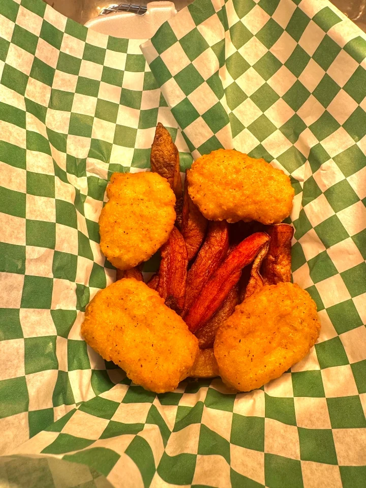 A serving of fried food containing crispy nuggets and sweet potato fries in a basket lined with green and white checked paper.