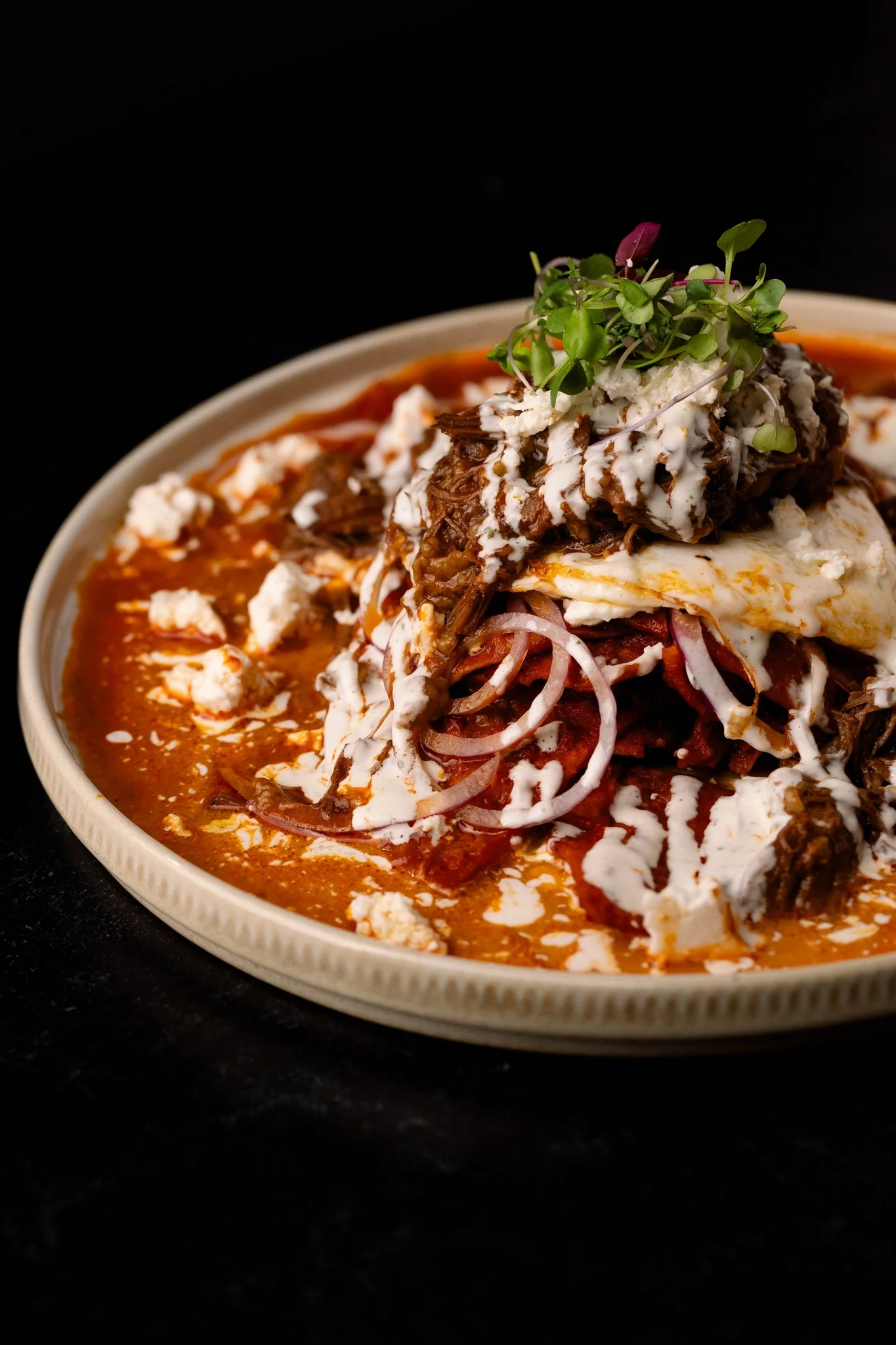 Plate of Mexican enchiladas topped with beef and crema