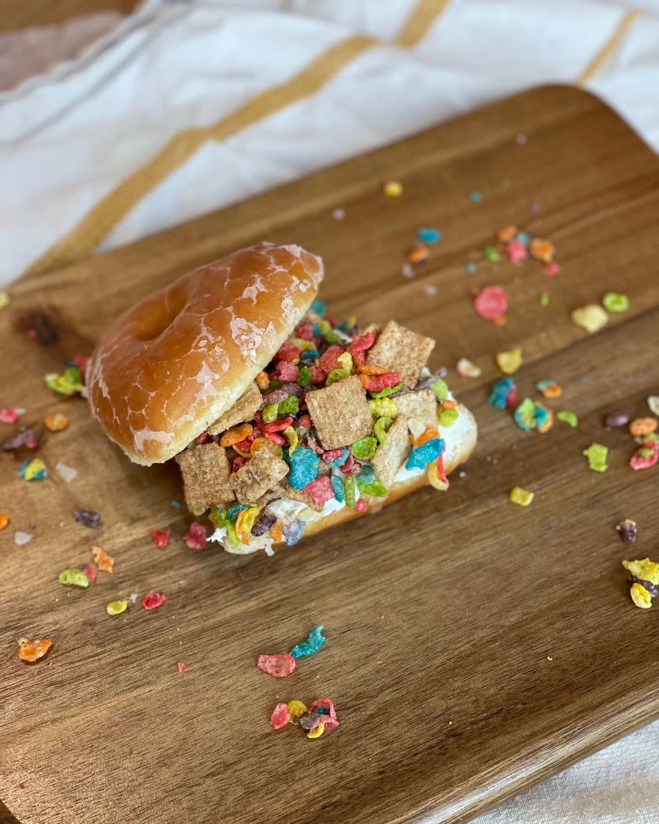 Creative donut topped with pretzels, M&M's, crushed cookies, and potato chips from BAD Bakery, displayed on a wooden surface.