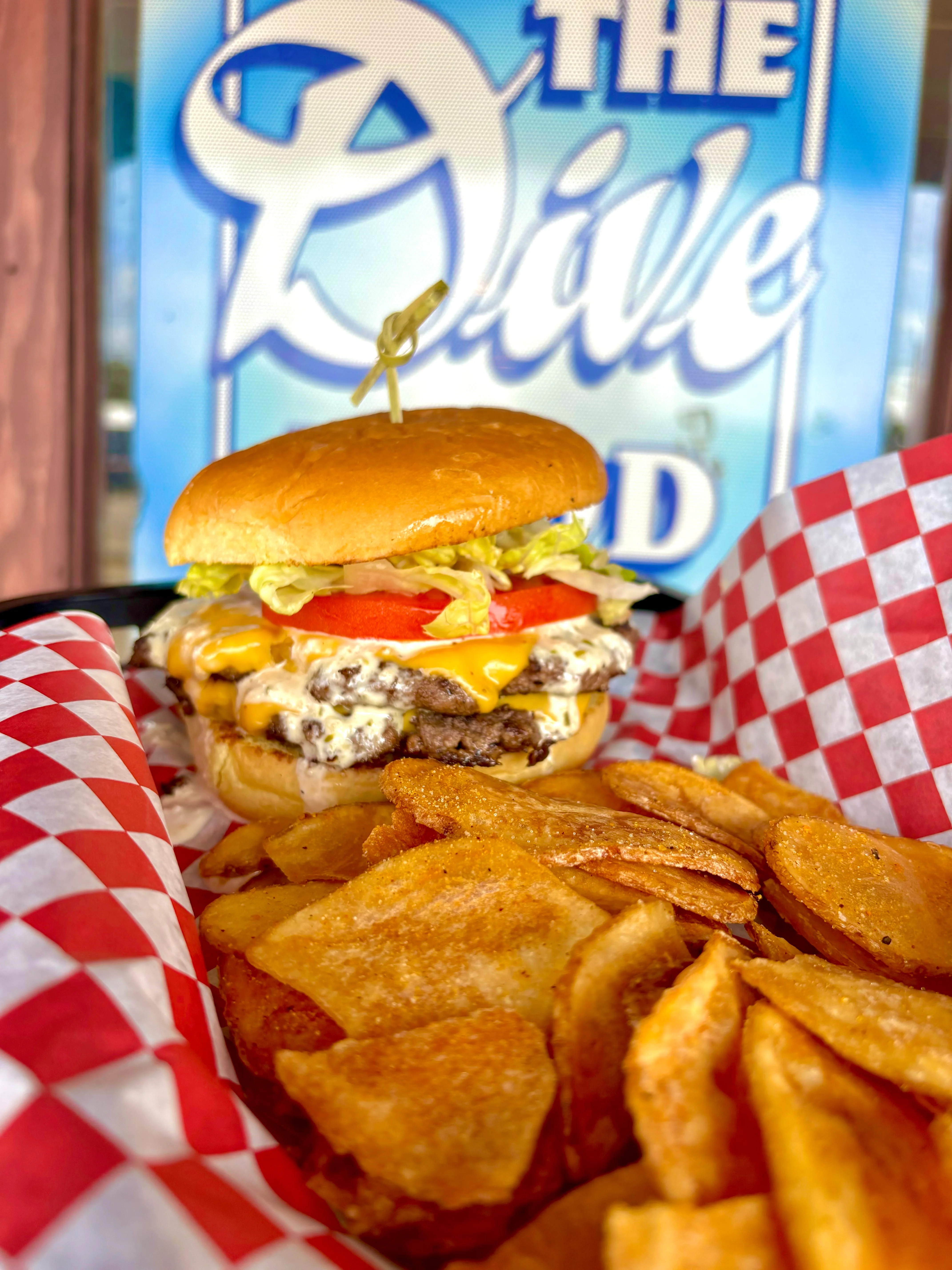 A delicious cheeseburger with lettuce, tomato, and two beef patties served with a side of homemade potato chips.