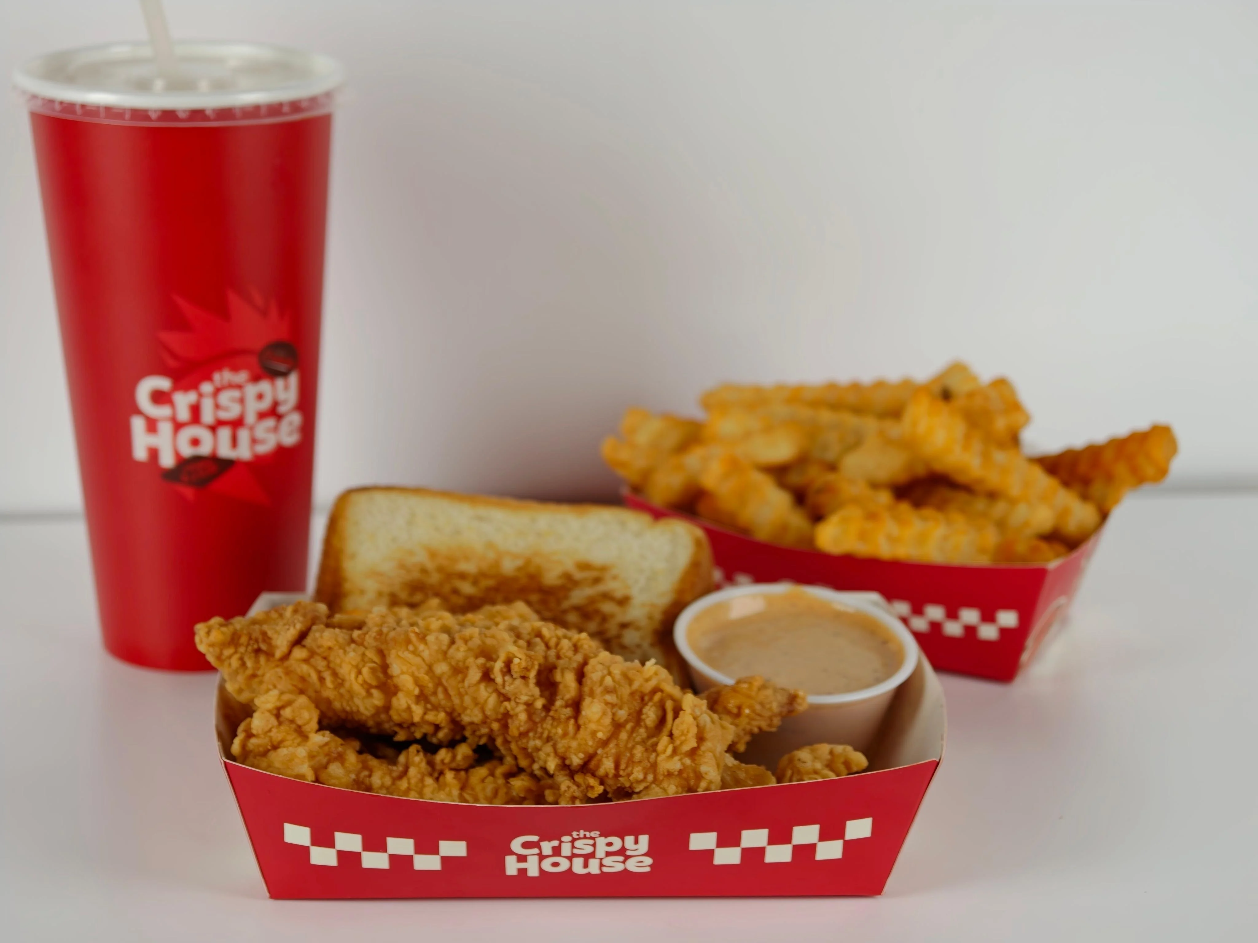 A serving of crispy fried chicken tenders on a tray with crinkle-cut fries, a slice of bread, and dipping sauce.