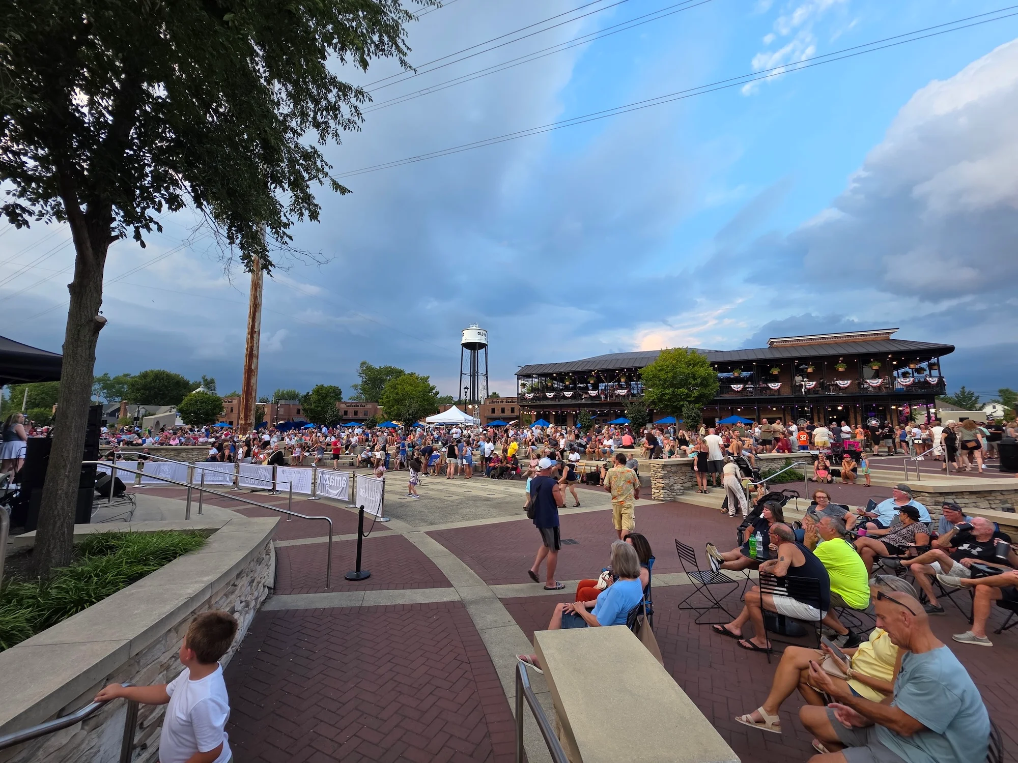 A crowded outdoor event featuring a diverse audience gathered for a performance, set against a backdrop of a historic building.