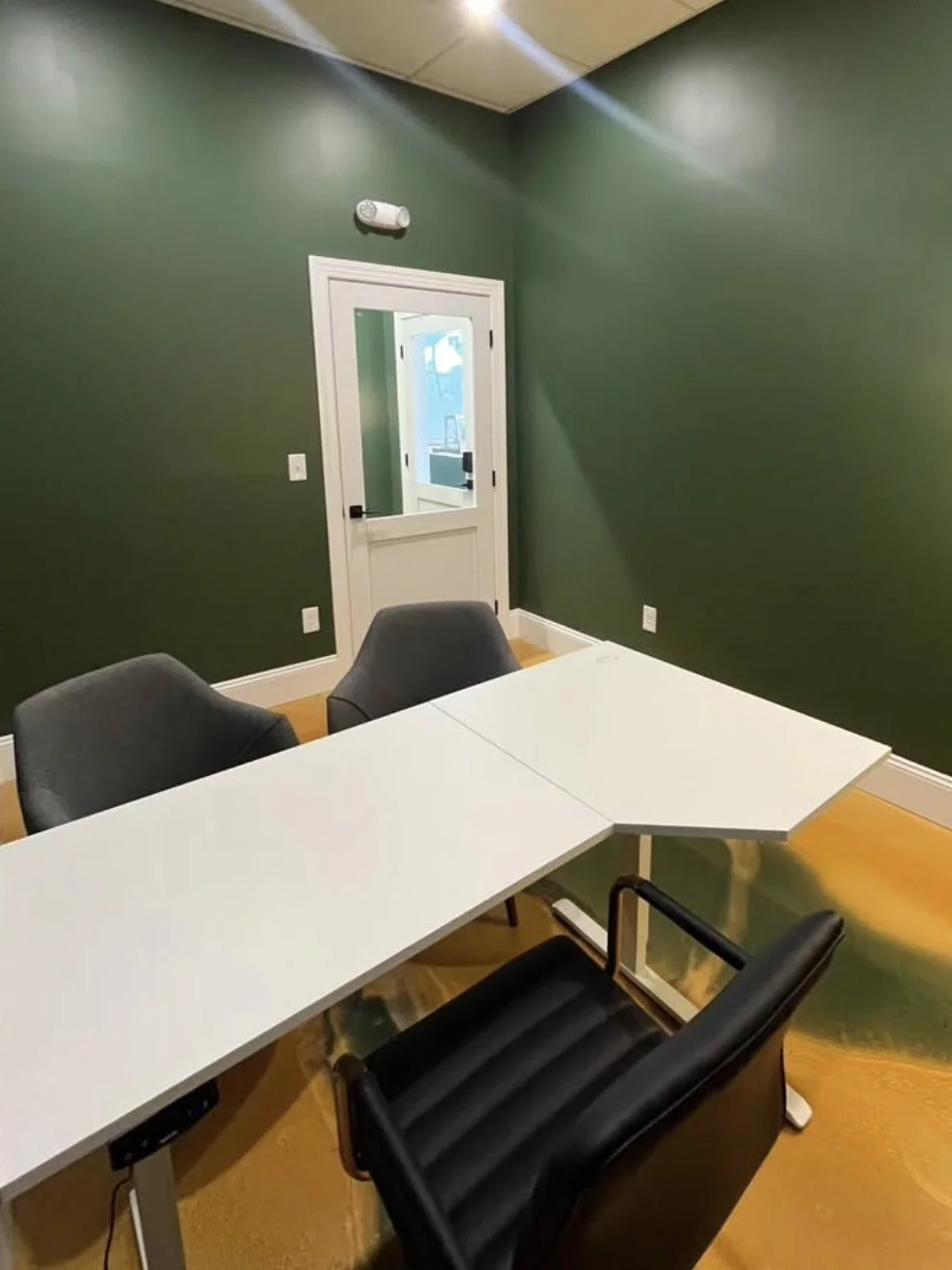A large wooden conference table surrounded by black rolling chairs in a modern meeting room.