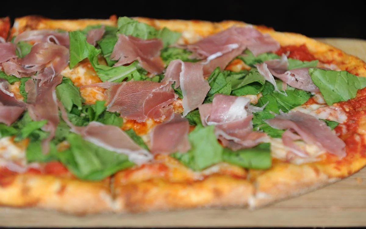 Italian prosciutto pizza topped with fresh greens