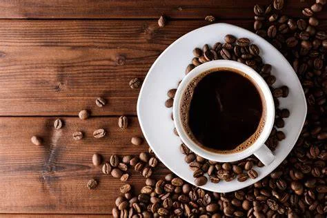 Cup of freshly brewed coffee surrounded by coffee beans on wooden table