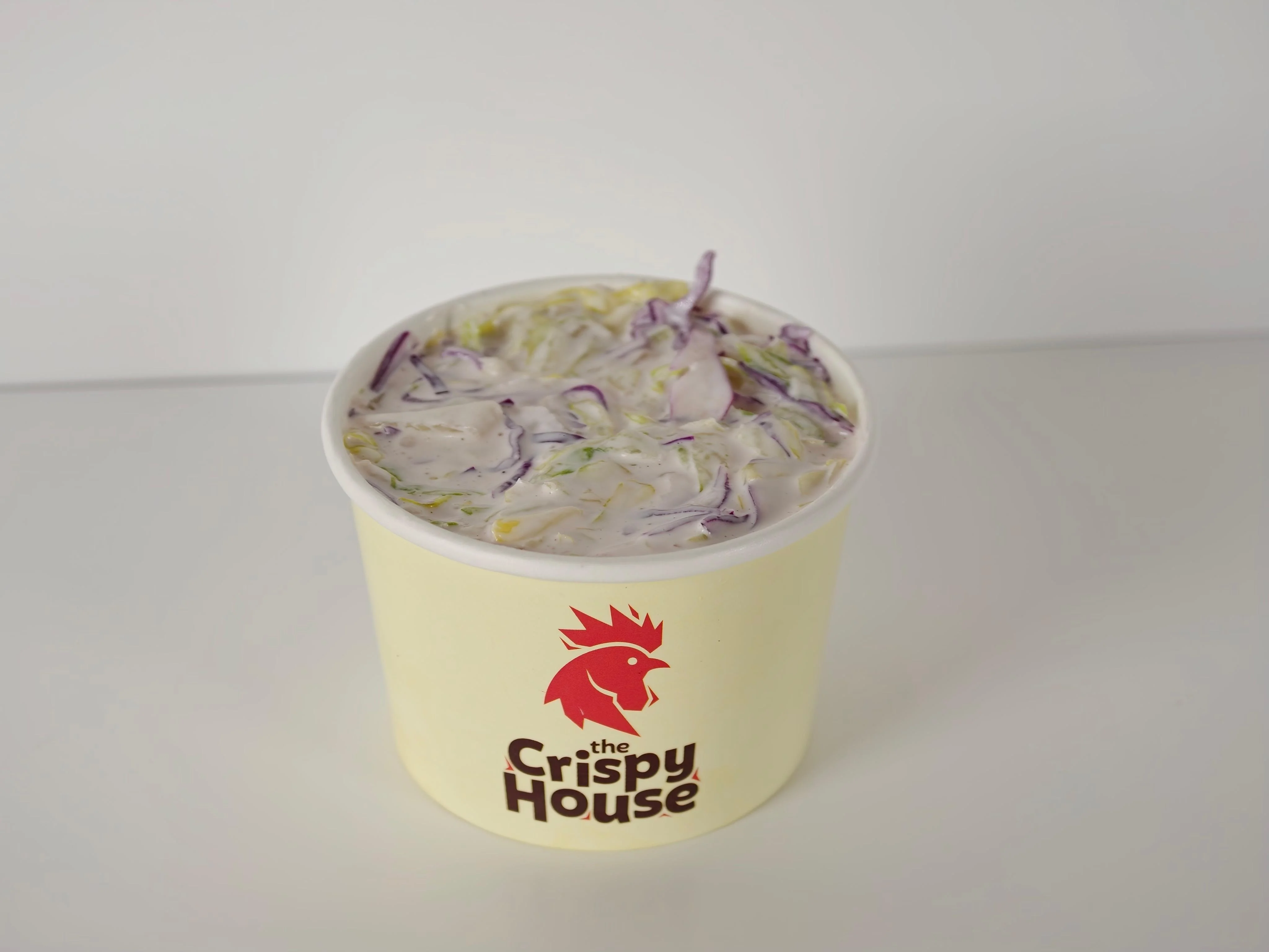 A cup of coleslaw featuring a mix of cabbage with a creamy dressing, branded with a logo.