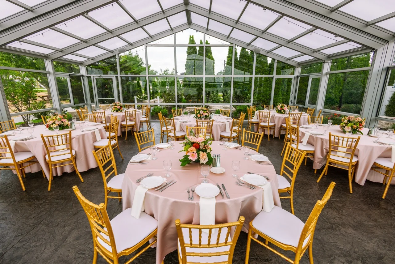 A glass atrium with tables, pink linens and a beautiful sky as the backdrop
