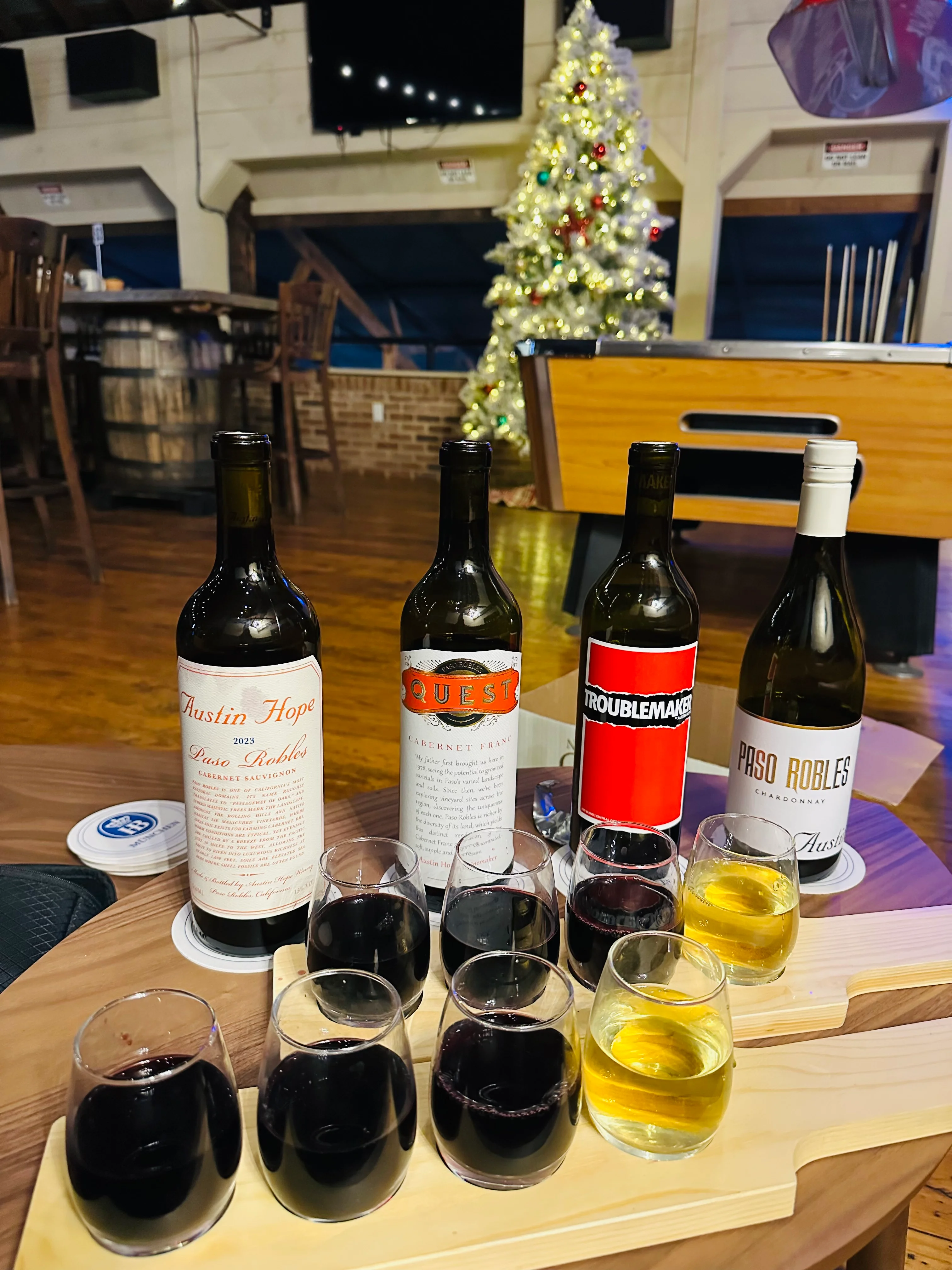 A selection of wines presented in tasting glasses with a Christmas tree and bar scene in the background.