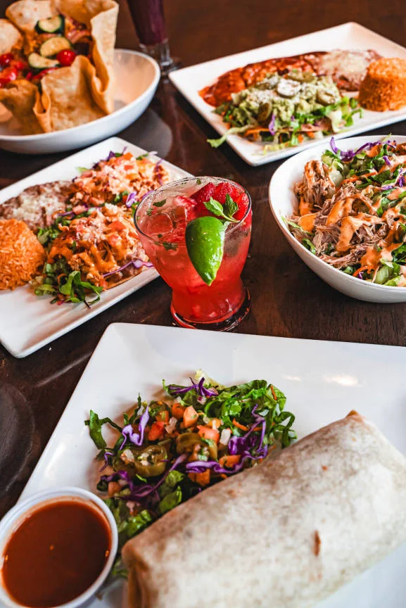 Colorful Mexican feast with burrito, tacos, and refreshing cocktail