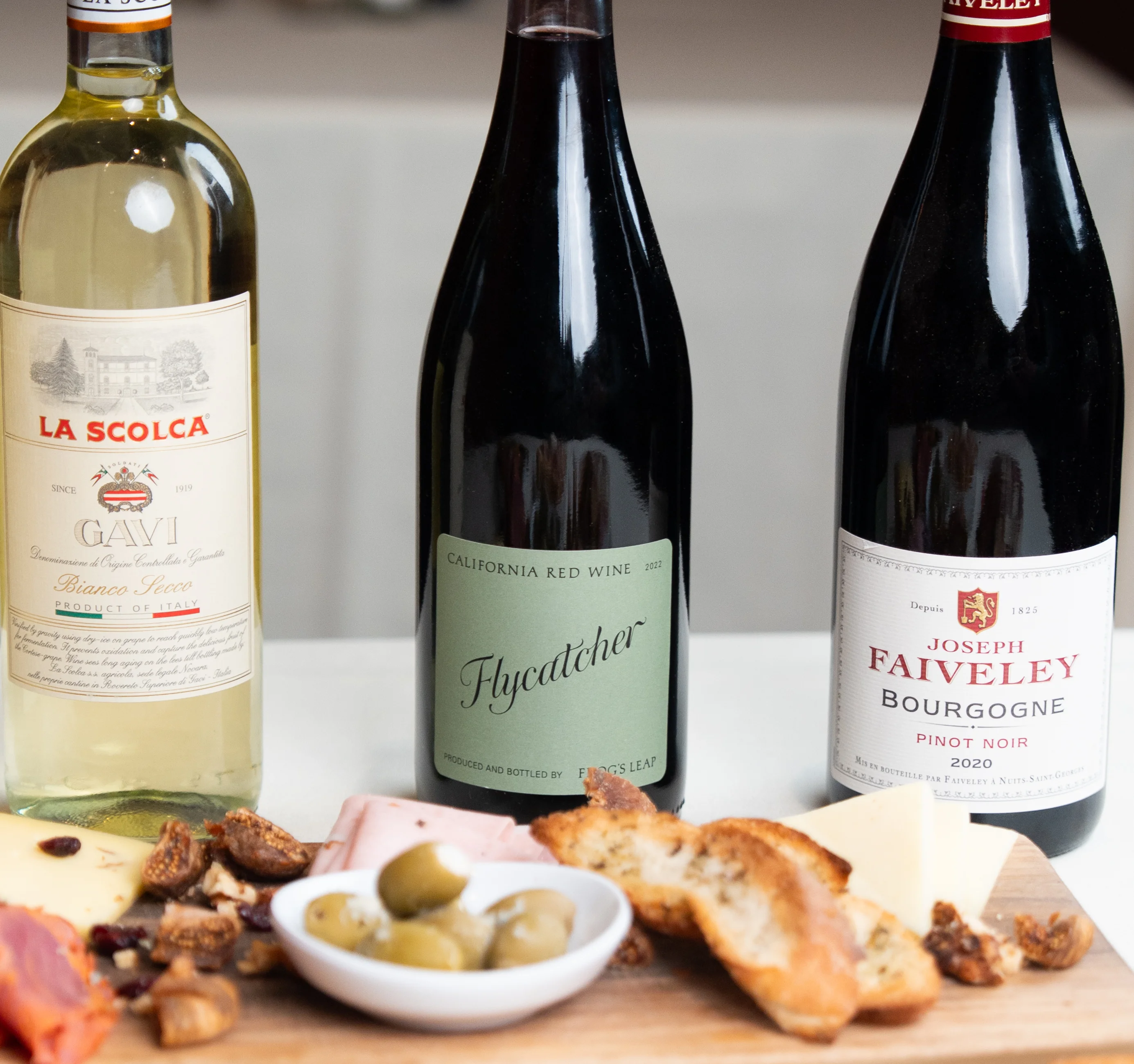 Three wine bottles with a charcuterie board featuring meats and olives.
